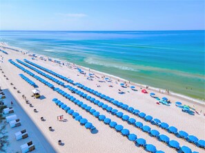 A beach with rows of blue umbrellas and white beach chairs, a sandy shore, and the ocean in the background. - Calypso Tower 3 by Panhandle Getaways (Panama City Beach)