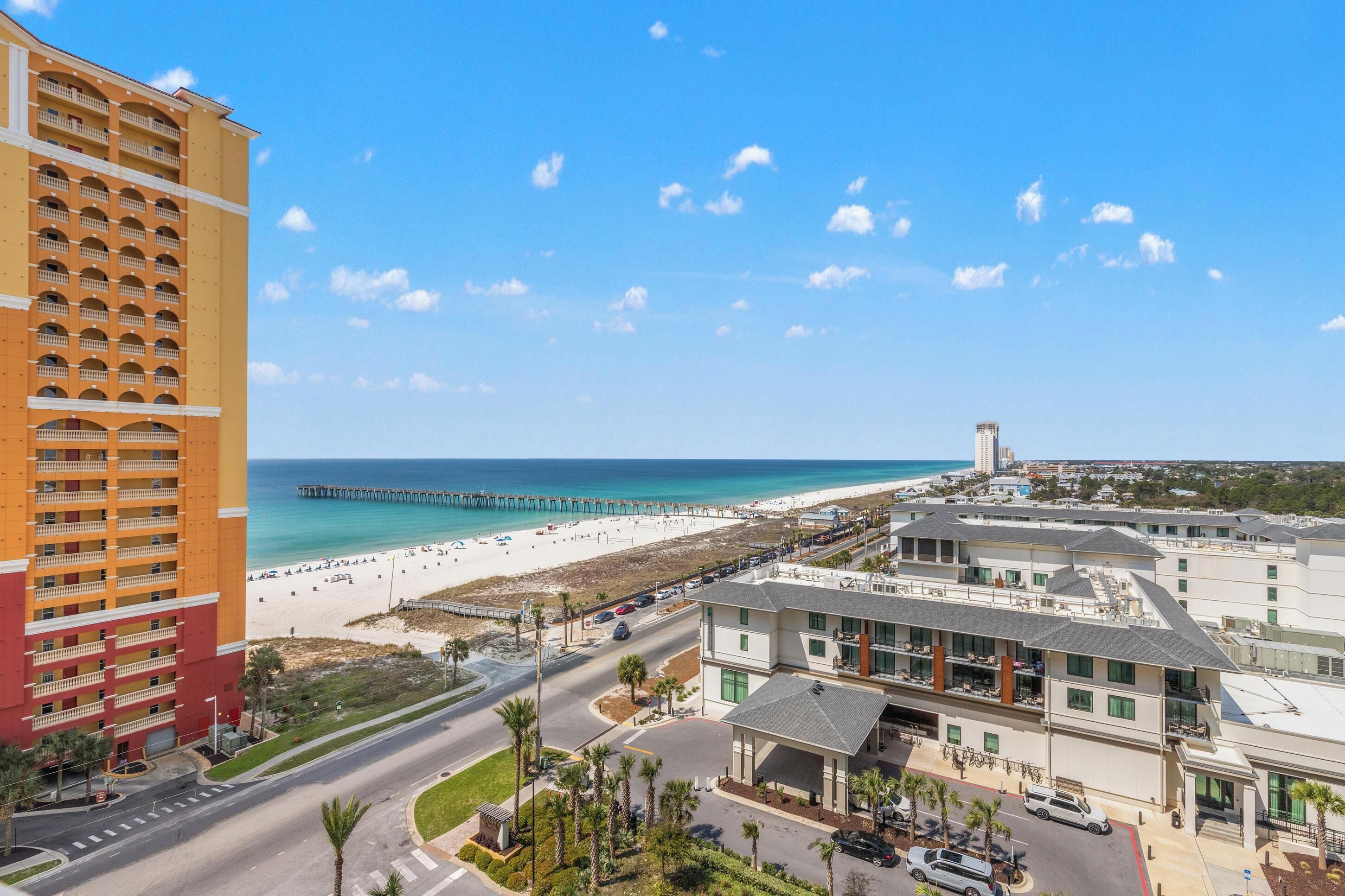 Un hotel frente al mar con vista a la playa, un muelle y un edificio alto a lo lejos.