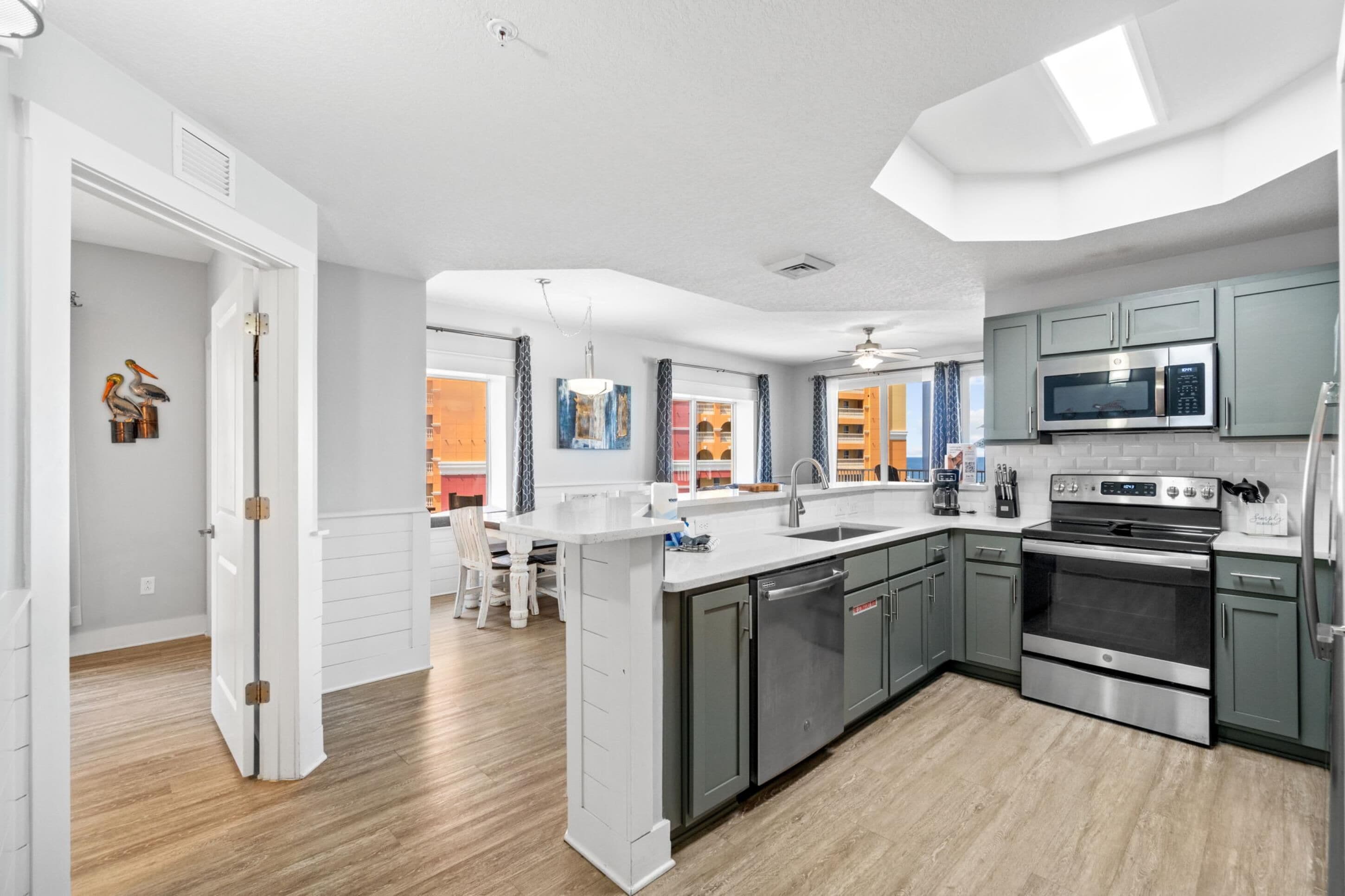 A modern kitchen with grey cabinets, stainless steel appliances, and a white countertop.