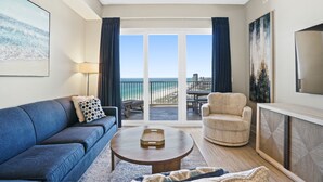 A living room with a blue sofa, a round coffee table, a patterned armchair, and a TV on a wooden cabinet.