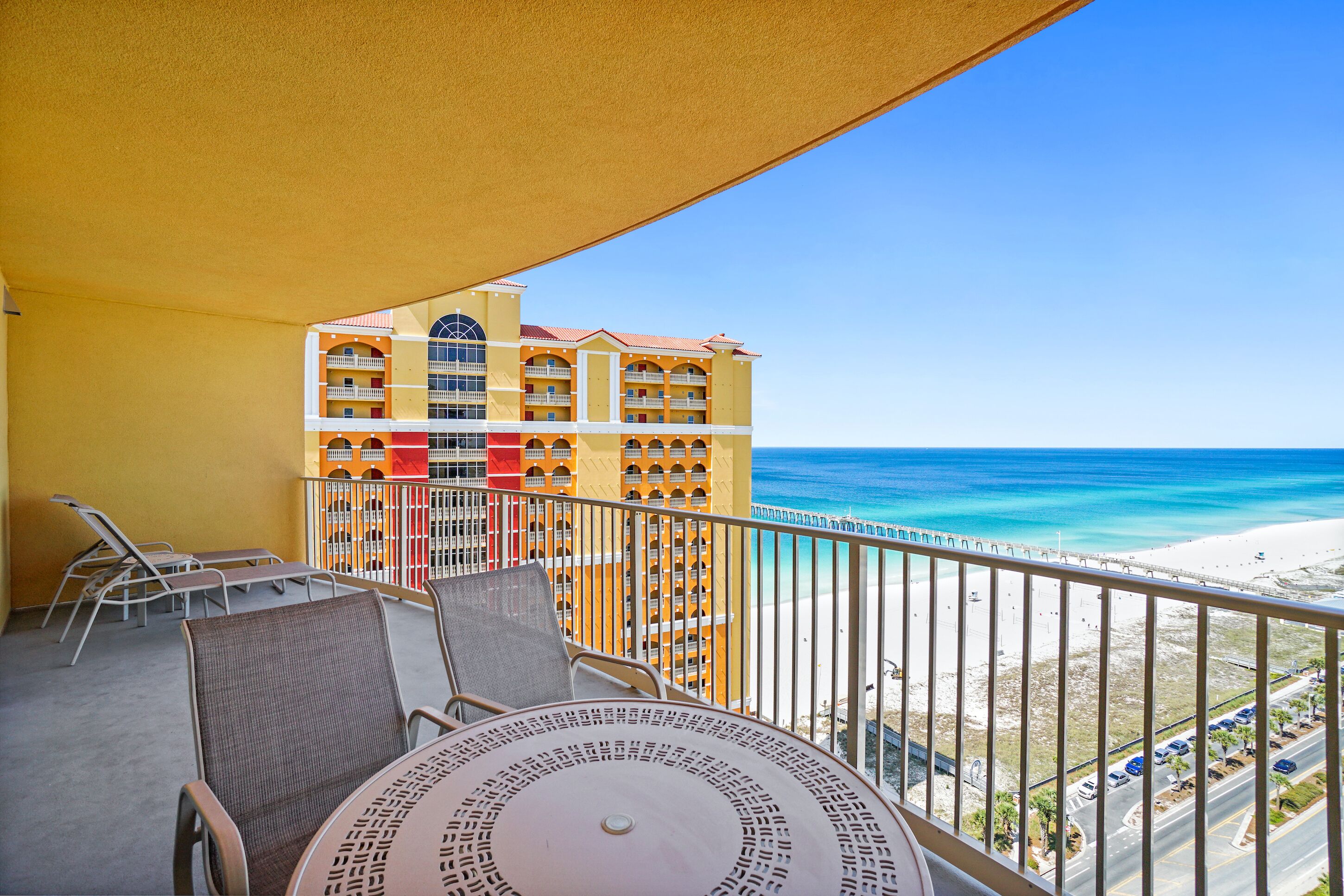 Un balcon aménagé avec du mobilier d’extérieur, donnant sur une plage et un bâtiment d’hôtel.