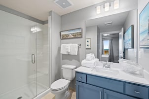 A modern bathroom with a glass shower enclosure, a white toilet, a vanity with a mirror, and a view of the city.