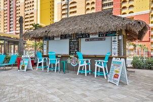 A tiki bar with a thatched roof, a menu board, and turquoise chairs.