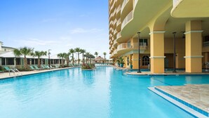 A hotel pool area with a clear blue pool, lounge chairs, and a multi-story building with balconies.