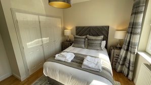 A bedroom with a bed, two bedside tables, a headboard, a window with curtains, and a door.