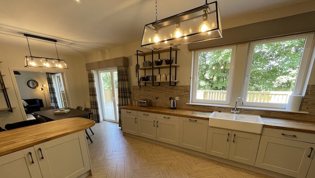A modern kitchen with herringbone wood flooring, white cabinetry, a wooden countertop, and a large window with a view of greenery.