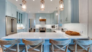 Une cuisine moderne avec des meubles de couleur bleu clair, un grand îlot central doté de tabourets, des appareils en acier inoxydable et un éclairage suspendu.