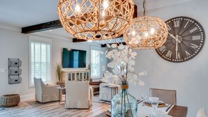 Un espace repas comprenant une table en bois, des chaises, une grande horloge murale et des luminaires sphériques suspendus.