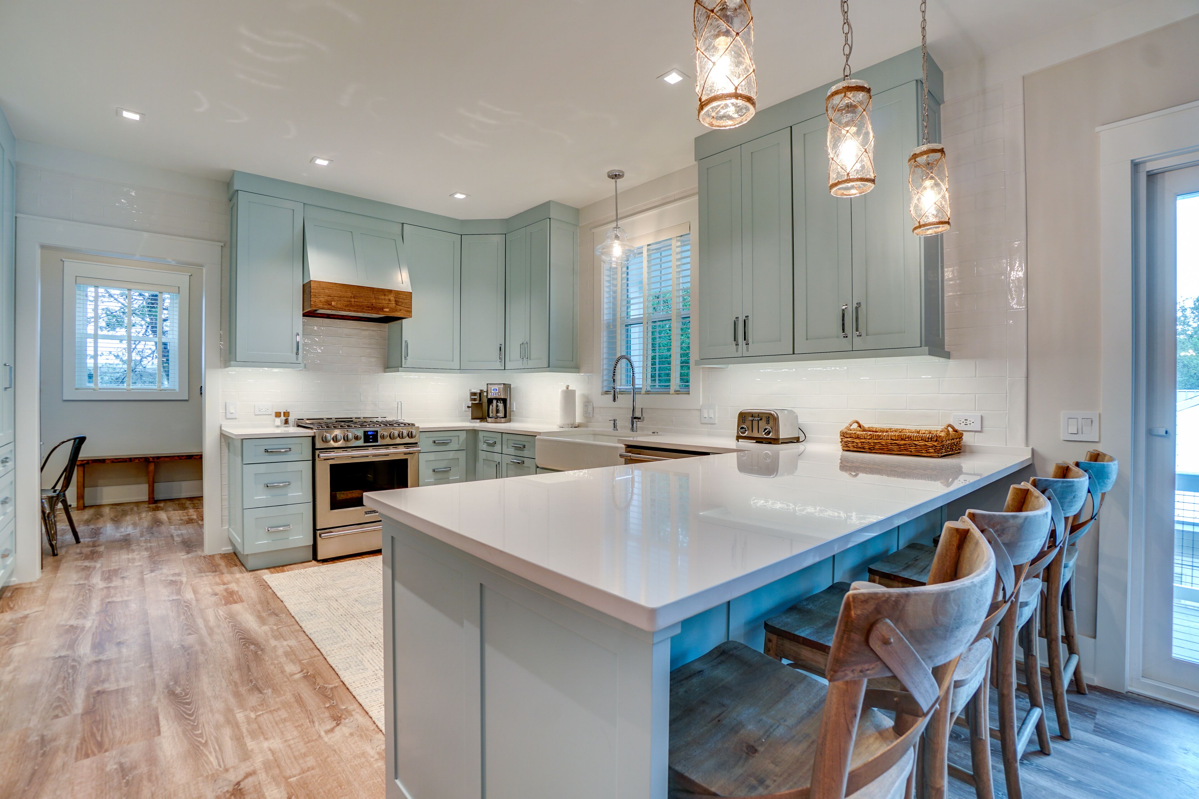 A modern kitchen with light blue cabinets, a large island, wooden bar stools, and pendant lighting.