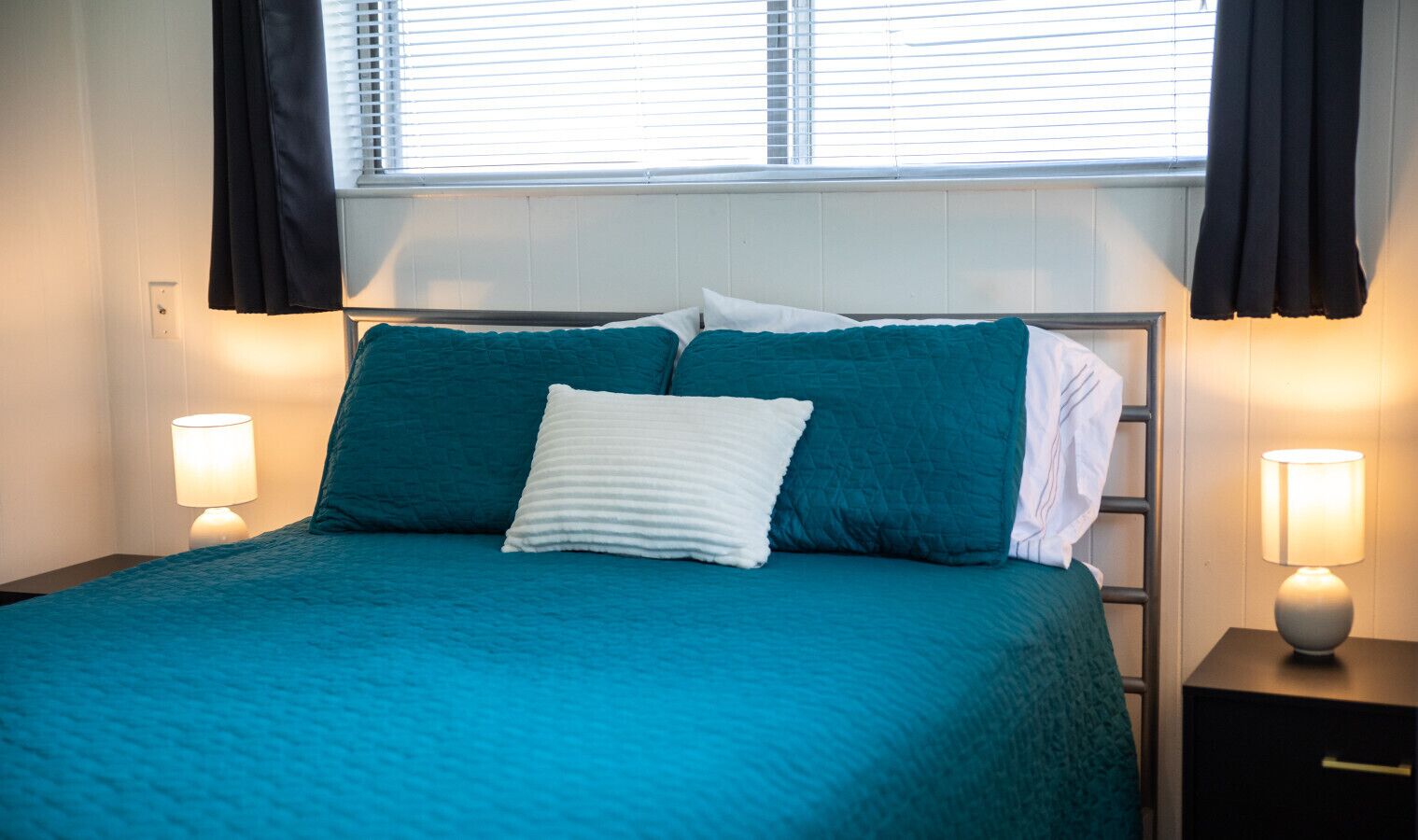 A bed with teal bedding and white pillows, flanked by two bedside lamps.