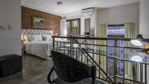 Ein Schlafzimmer mit Bett, Schreibtisch, Stuhl, einer Treppe und Blick nach draußen.