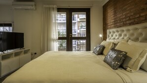 A hotel room with a large bed, a television, and a view of a brick wall and balconies outside. - Loft Premium DE Primer Nivel (Ciudad Autónoma de Buenos Aires, Recoleta)