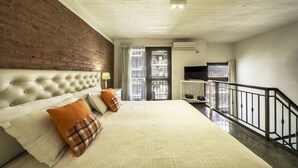 A bedroom with a brick wall, a tufted headboard, a large bed, a TV, and a balcony. - Loft Premium Imperdible (Ciudad Autónoma de Buenos Aires, Recoleta)