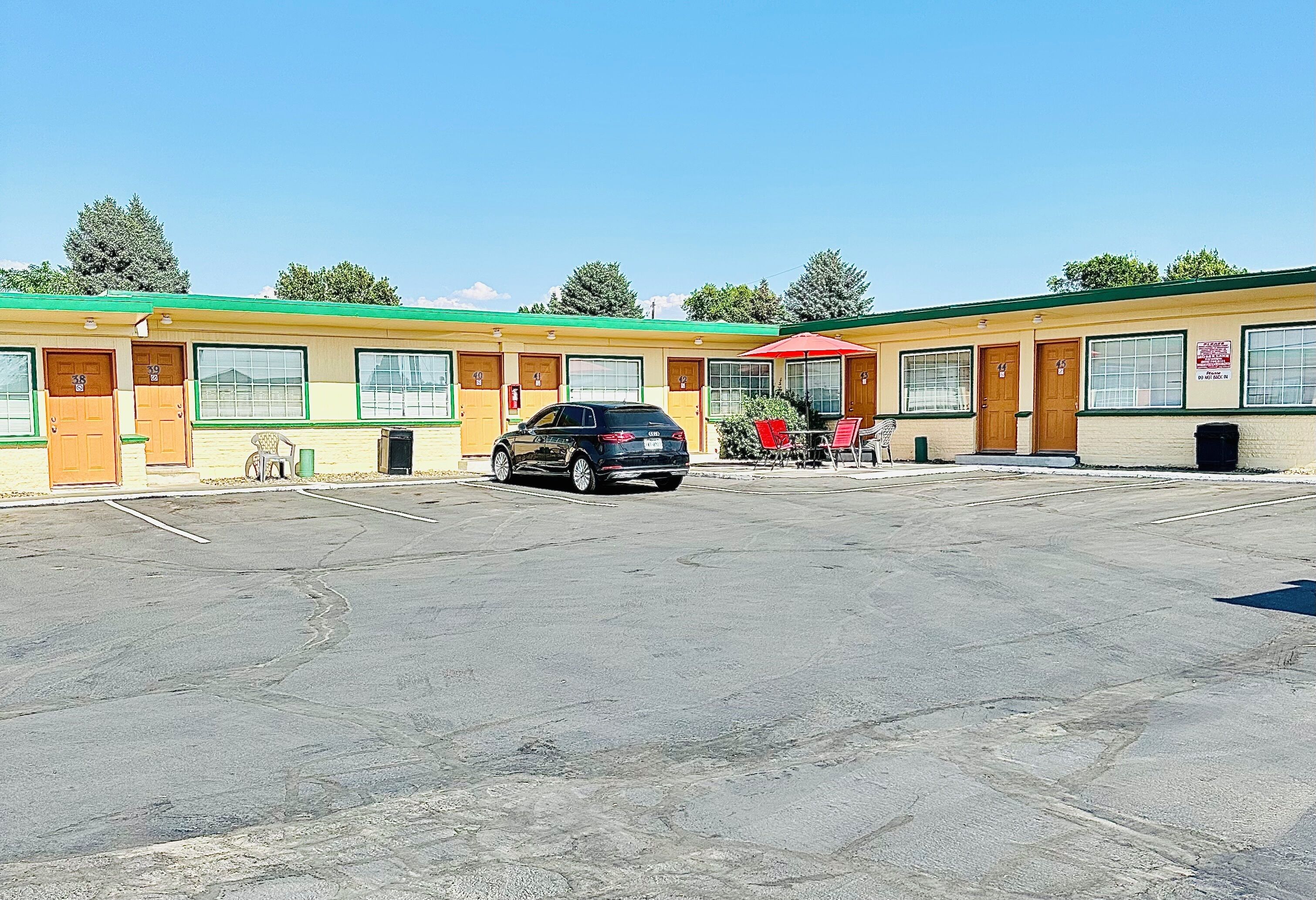 Een motel met meerdere kamers, een parkeerplaats en een rode paraplu.