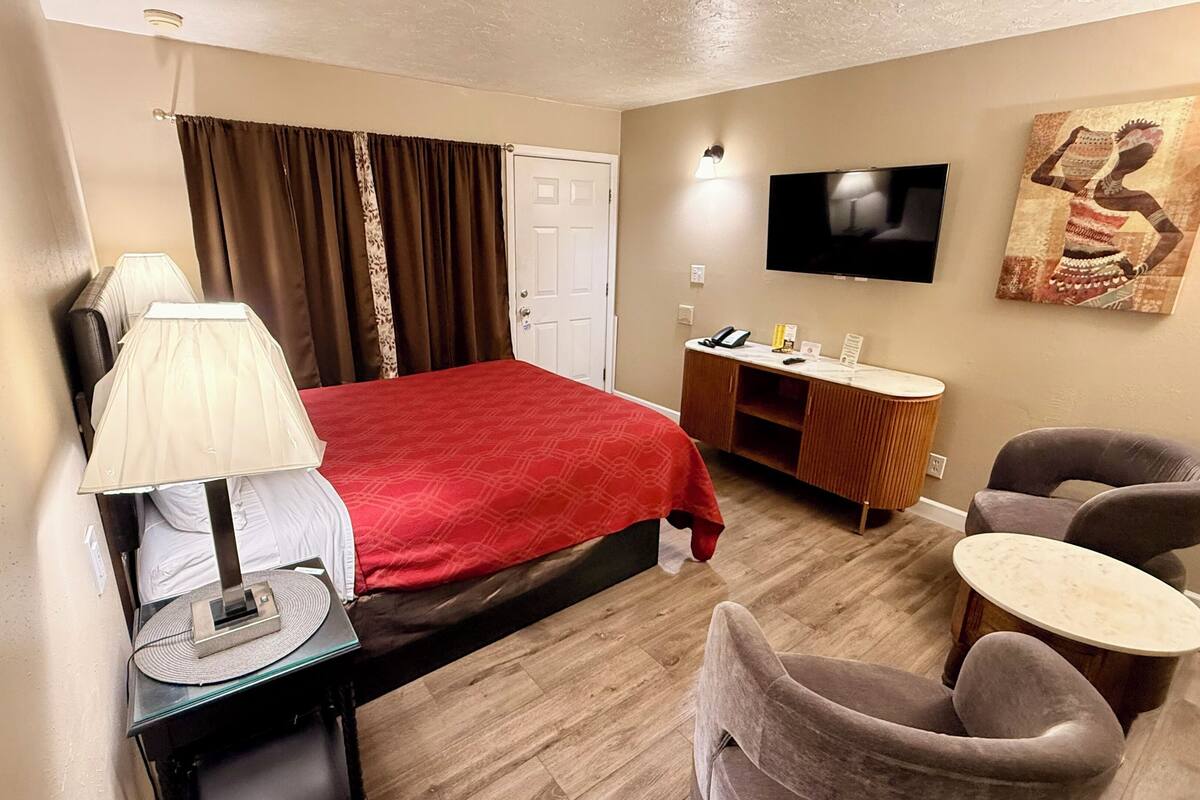 A hotel room with a bed, desk, chair, TV, and artwork on the wall.
