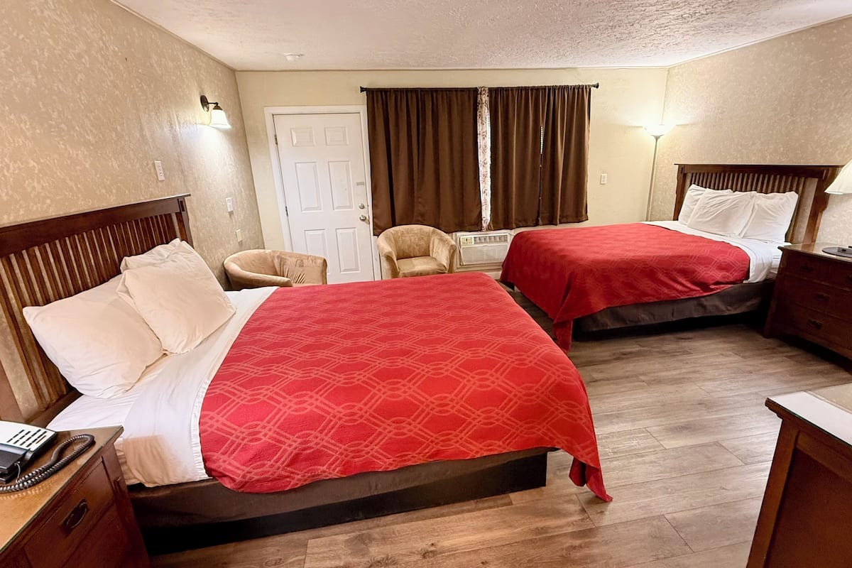 A hotel room with two beds, a chair, a desk with a phone, and a lamp.