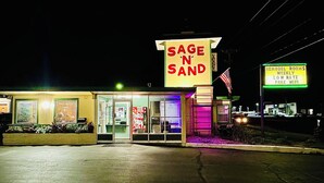 A building with a prominent 'Sage N' Sand' sign, a coffee shop, and a neon sign advertising 'Remodel Rooms' with 'Weekly Low Rate Free WiFi'. - Sage N Sand Motel (Moses Lake)