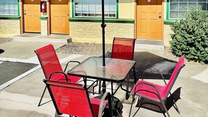 A hotel with a red umbrella, numbered doors, and outdoor seating. - Sage N Sand Motel (Moses Lake)