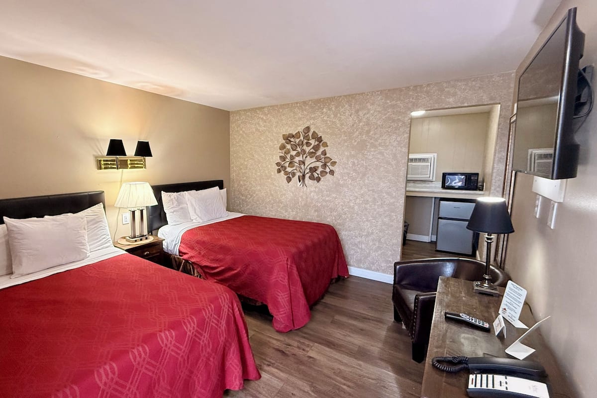 A hotel room with two beds, a desk, a chair, a mirror, and a wall-mounted decorative piece.