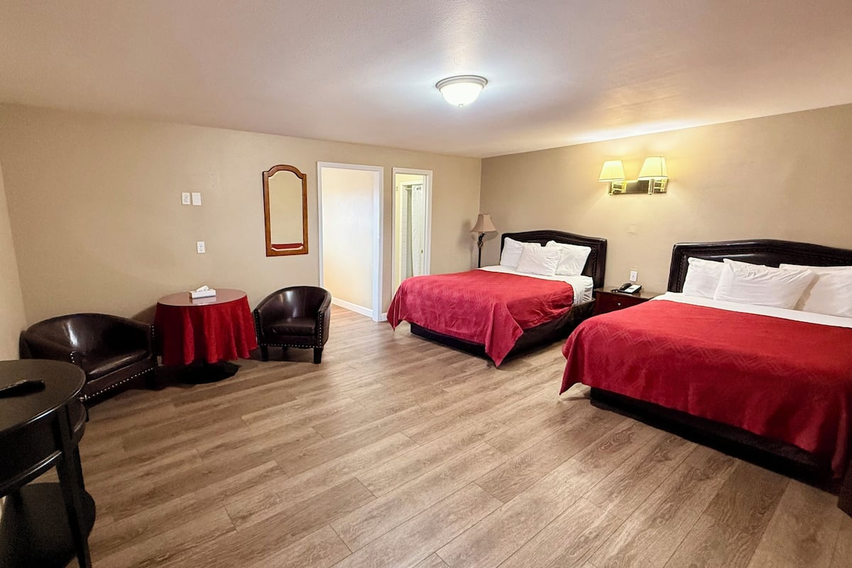 A hotel room with two beds, a desk, a chair, a TV, and a door leading to a bathroom.