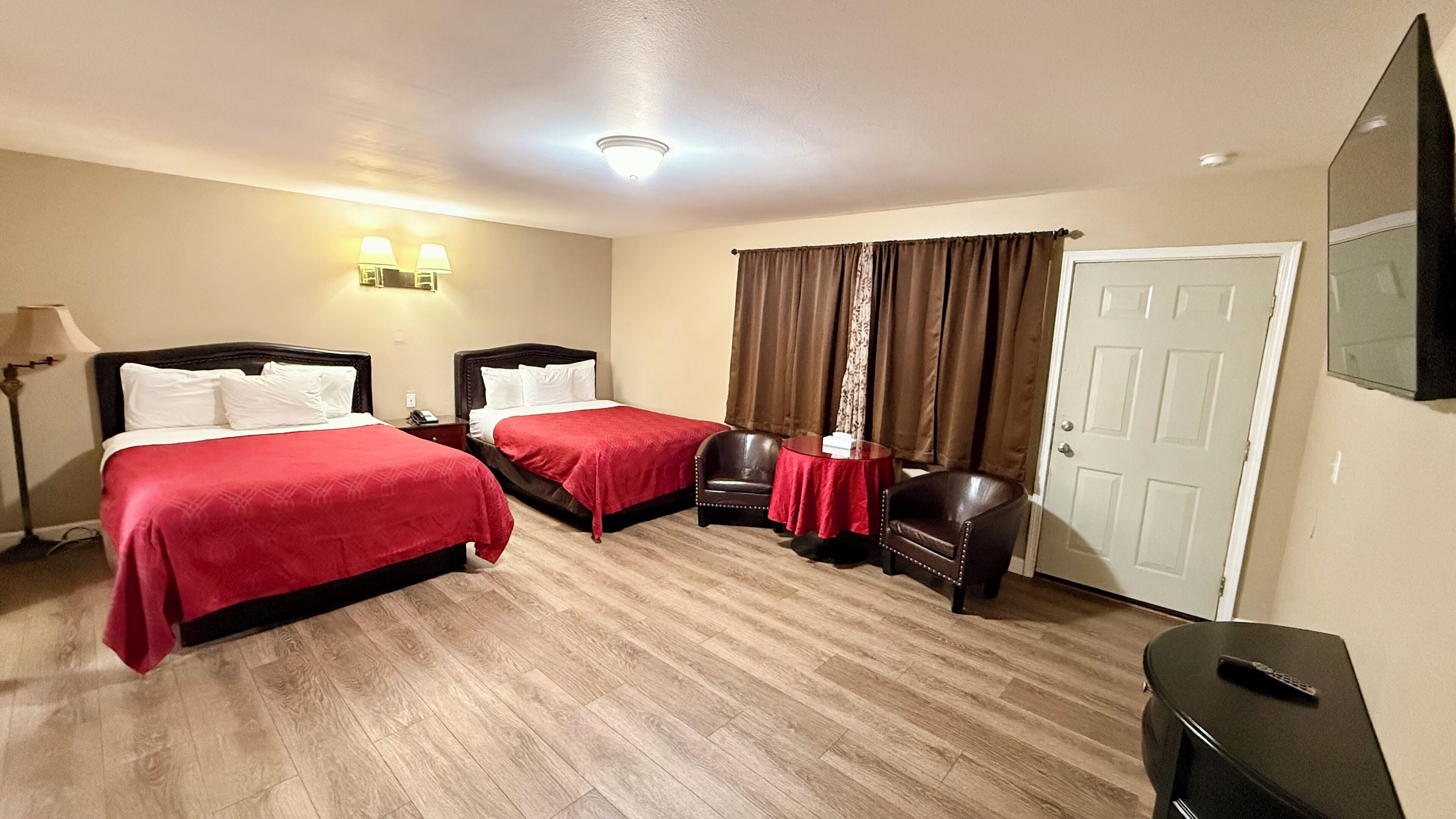 A hotel room with two beds, a desk, a chair, a TV, and a door.