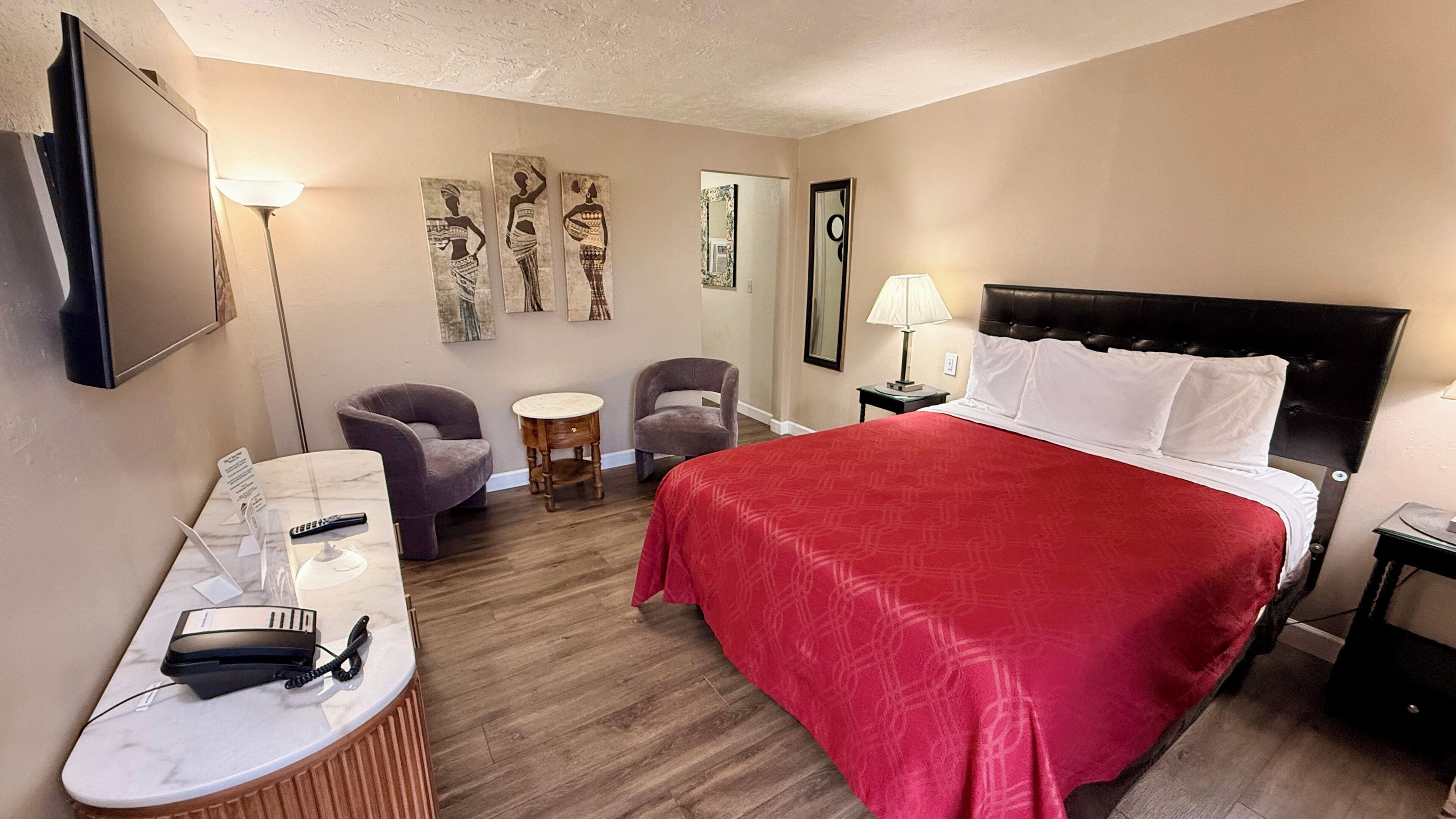 A hotel room with a bed, two armchairs, a desk with a phone, and artwork on the walls.