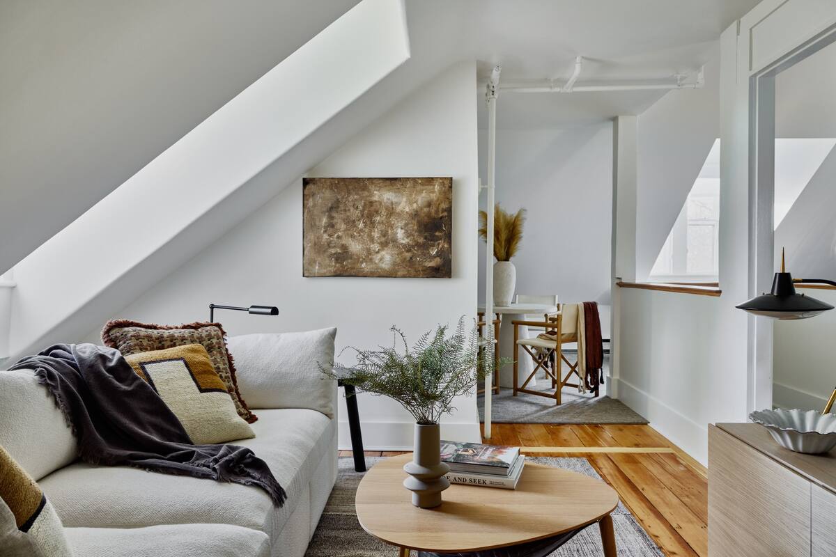Un loft modern amb sostre inclinat, una zona d'estar acollidora amb un sofà i una taula de centre, i una zona de dinar amb una cadira i una taula.