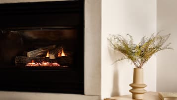 A modern fireplace with logs, a vase with greenery, and a woven chair.