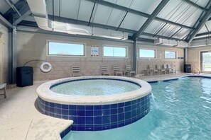 An indoor swimming pool with a hot tub, tiled walls, and windows.