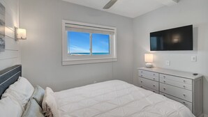 Un dormitorio con cama, tocador, ventilador de techo, televisión y ventana con vistas.