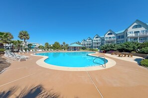 A resort with a large swimming pool, lounge chairs, and a building with multiple balconies.