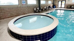 Una piscina interior con jacuzzi, paredes de azulejos y ventanas.