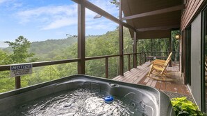 Ein Whirlpool auf einer Holzterrasse mit Blick auf einen Wald. Ein Schild warnt davor, sich auf die Brüstung zu setzen oder darauf zu klettern.