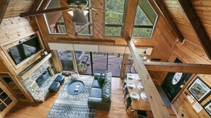 Eine Holzhütte mit hohen Decken, einem Kamin aus Stein, einer Couch und einem Essbereich.