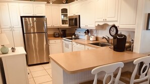 A modern kitchen with white cabinetry, stainless steel appliances, and a central island with chairs. - OCEANFRONT 2 BR CONDO! PANORAMIC OCEAN VIEWS FROM LIVING ROOM AND BEDROOMS  (Fort Pierce)