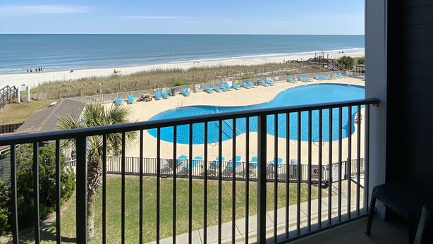 A balcony with a view of a beach and a pool.