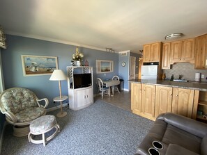 A living room with a television, a dining area with a table and chairs, and a kitchen with wooden cabinets and a refrigerator. - Myrtle Beach Resort-Direct oceanfront- free waterpark/grills-Recently updated! (Myrtle Beach)