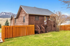 Ein Holzhaus mit einer Treppe, die zu einer Veranda führt, umgeben von einem Holzzaun und einem Rasen.