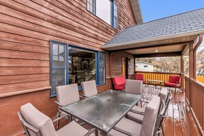 Eine überdachte Terrasse mit Tisch und Stühlen, ein Holzhausfassade und der Blick auf ein Nachbarhaus.
