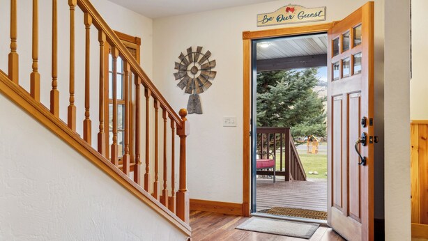 Eine Holztreppe führt zu einer Tür mit einem Schild 'Be Our Guest', einer Windmüllerdeko und Blick auf eine Terrasse mit Gartenmöbeln.