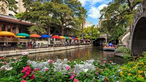 A riverside walkway with outdoor seating and umbrellas, a bridge, and a boat. - EILAN HOTEL & SPA - 1 BR (San Antonio)