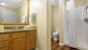 Un baño con tocador de madera, inodoro y zona de ducha.