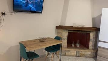 Ein Zimmer mit einem Holztisch und Stühlen, einem an der Wand befestigten Fernseher und einem Kamin mit einem 'WELCOME'-Schild.