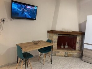 A room with a wooden table and chairs, a television mounted on the wall, and a fireplace with a 'WELCOME' sign. - Garden Square Inn (Markopoulo Mesogaias)