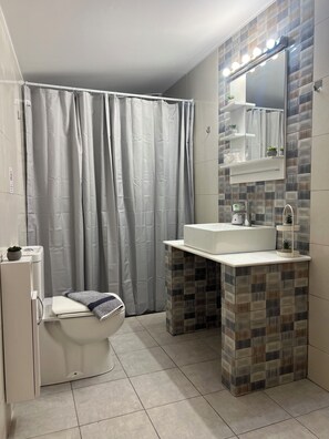 Un baño con inodoro, lavamanos con espejo, cortina de ducha y paredes de azulejos.