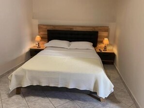 Una cama individual con cabecera de madera, dos mesitas de noche con lámparas y suelo de baldosas.