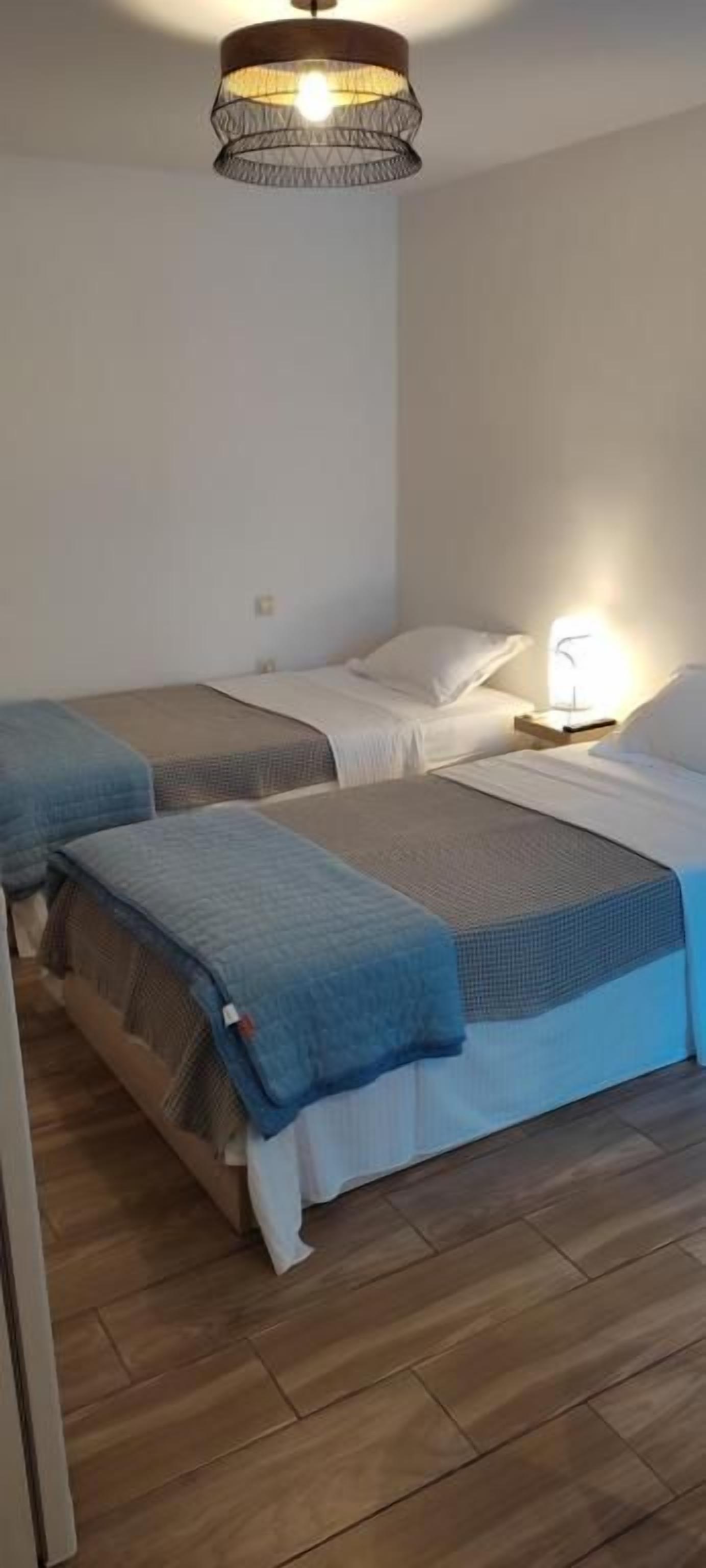 A room with two beds, a hanging light fixture, and a nightstand with a lamp.