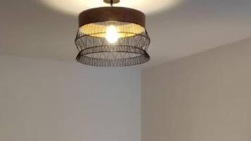 A room with two beds, a hanging light fixture, and a nightstand with a lamp.