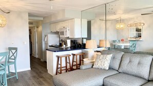 A modern kitchen with white cabinets, a central island with stools, and a dining area with a table and chairs. - Cozy Seaside Condo w/ Ocean Views - Pets Allowed! (St. Augustine)