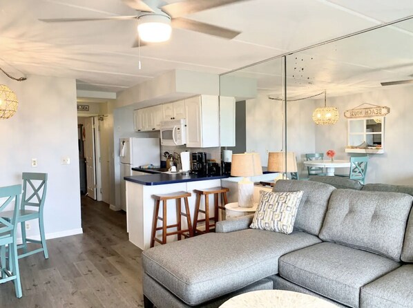 Una cocina moderna con gabinetes blancos, una isla central con taburetes y una zona de comedor con mesa y sillas.
